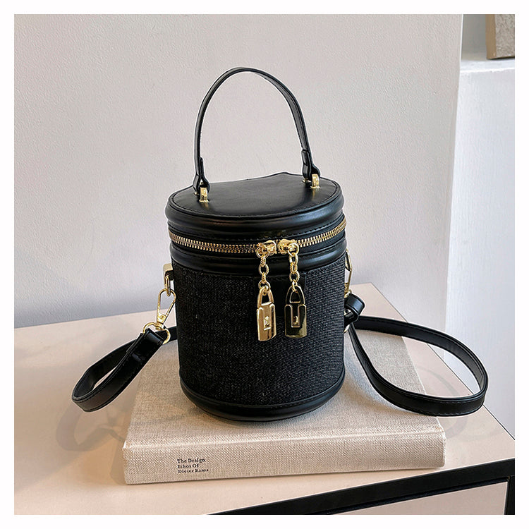 Handväska svart med cylinderform, dubbla dragkedjor och guldfärgade detaljer.