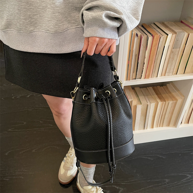 Svart bucket bag med lång axelrem buren i handen från Natta Collection.