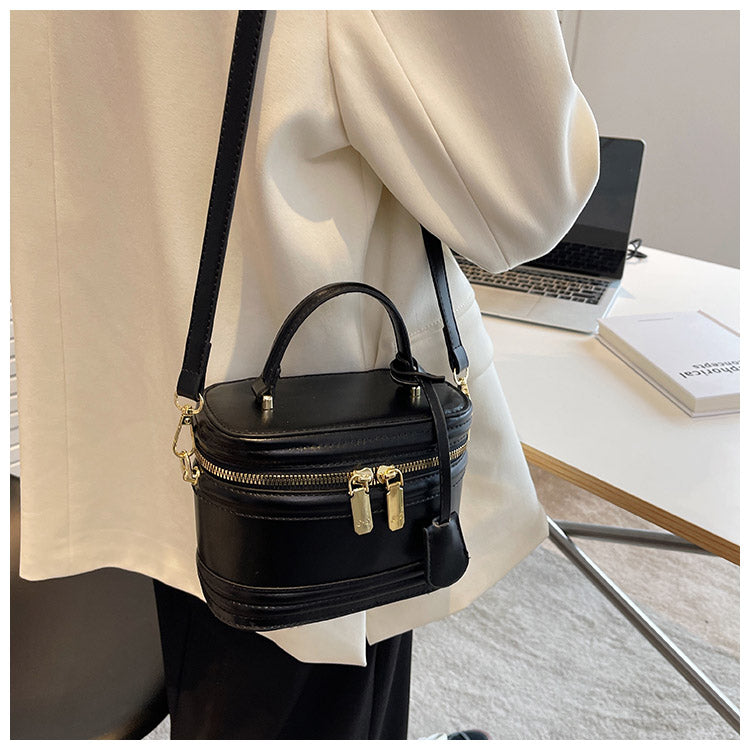 Handväska svart buren över axeln med justerbar axelrem och kompakt modell.