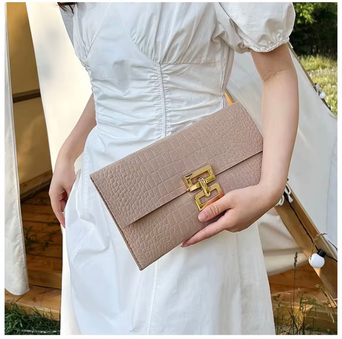 Nazar Bag beige kuvertväska med strukturerad yta och guldfärgat spänne, buren till vit klänning.