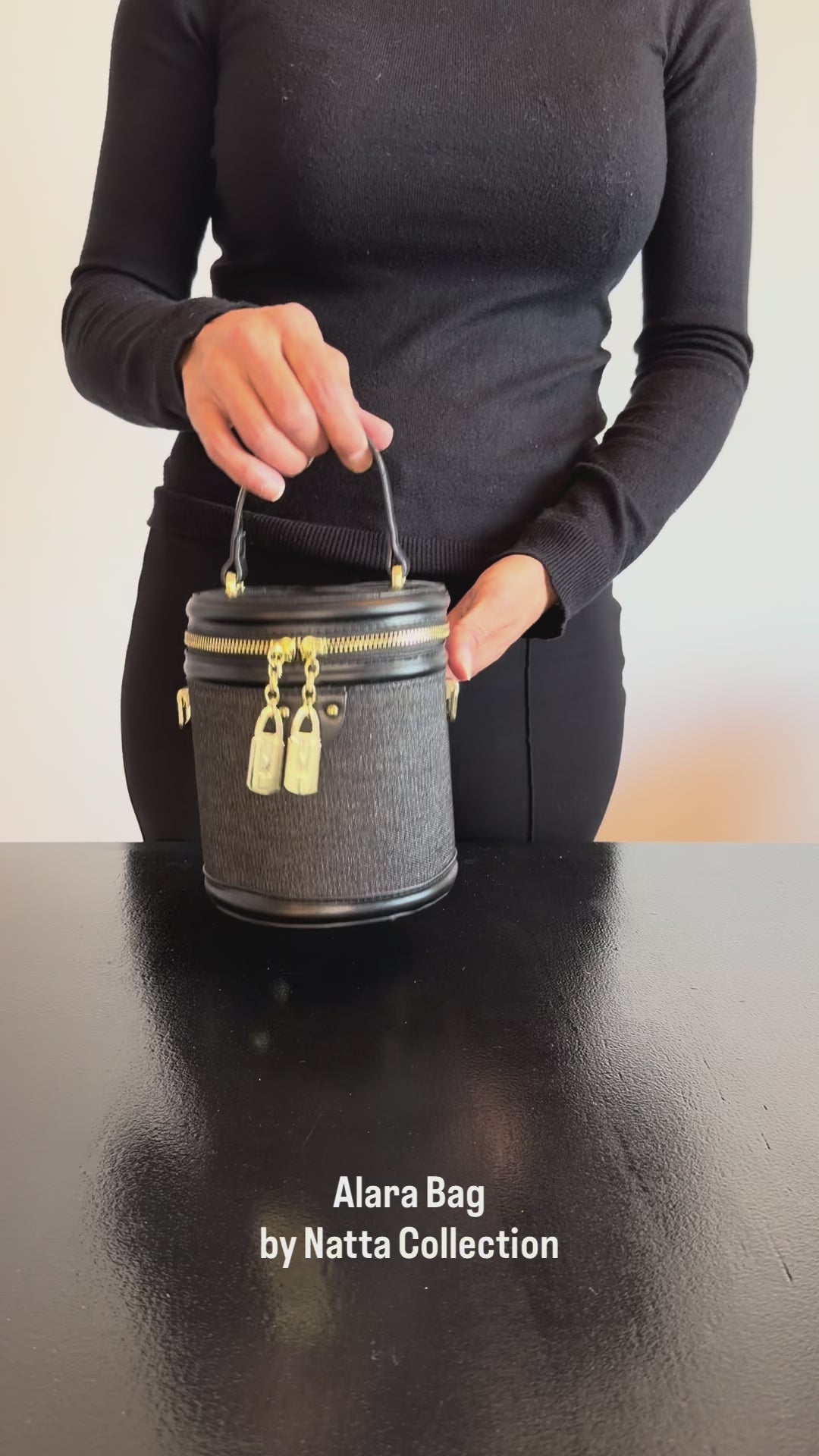 Produktvideo som visar Alara Bag i svart, en liten cylinderformad handväska med kort handtag, dubbla dragkedjor och guldfärgade detaljer, från olika vinklar och i närbild.