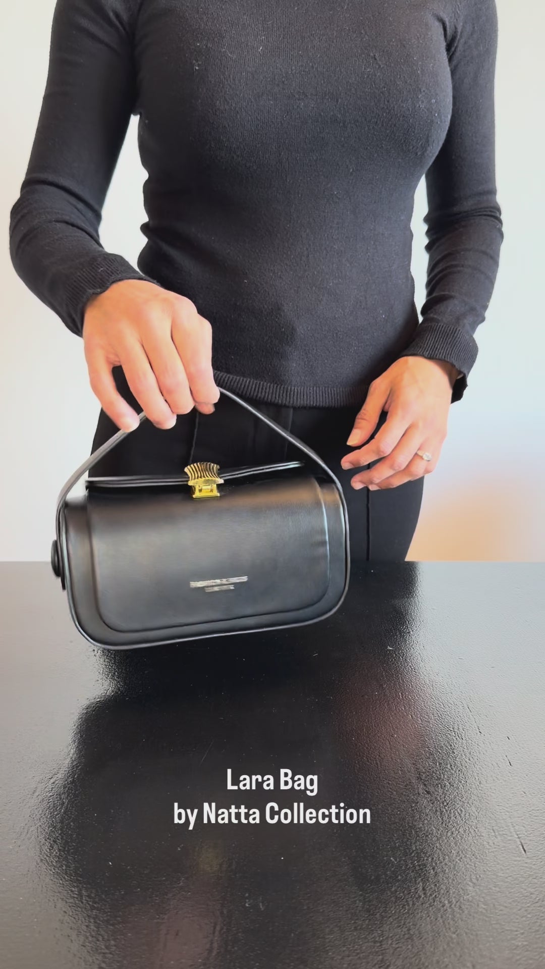 Produktvideo som visar Lara Bag i svart, en boxformad handväska med handtag och guldfärgad stängningsdetalj, från olika vinklar och i närbild.