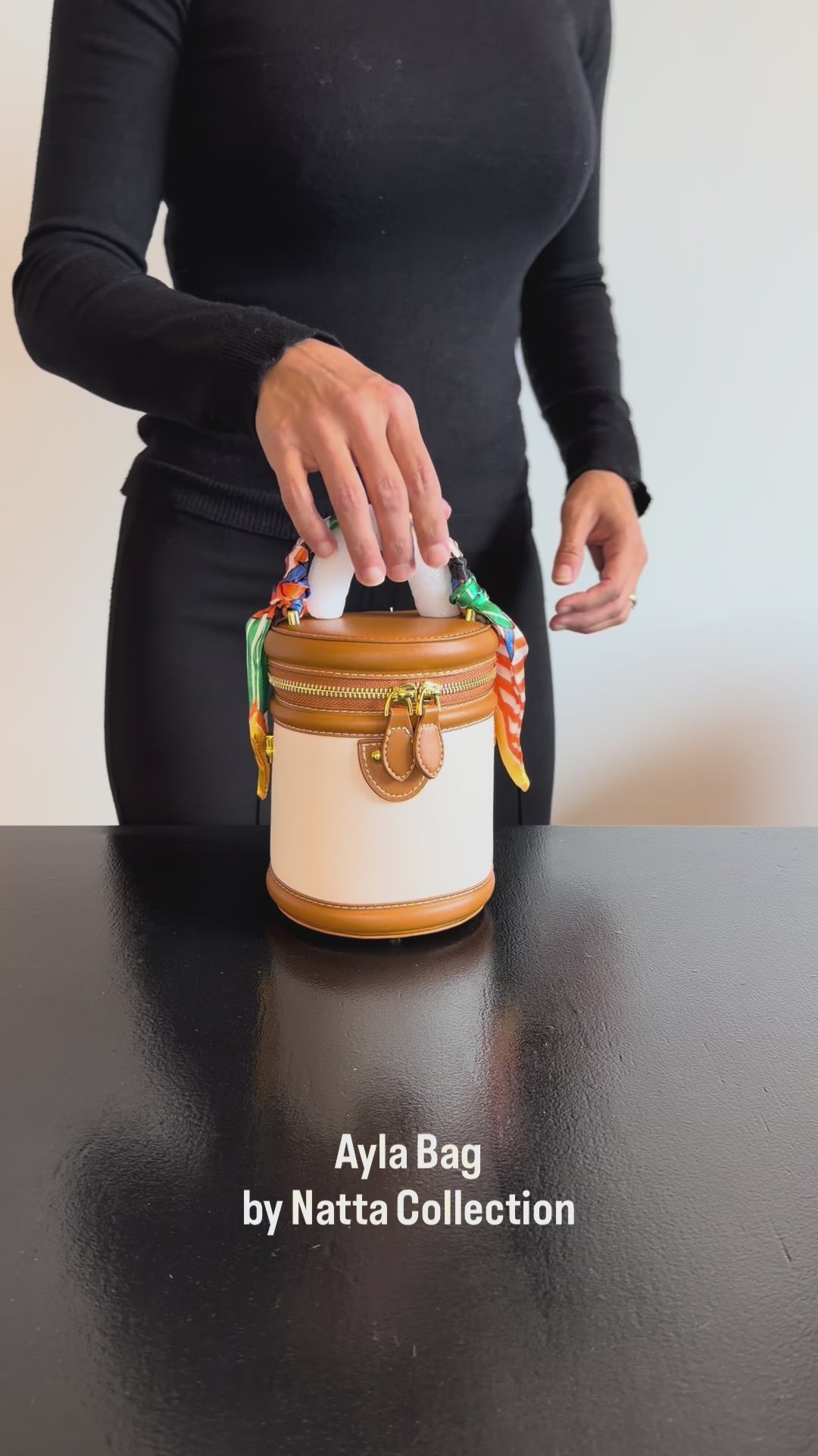 Produktvideo som visar Ayla Bag i beige och brun, en cylinderformad handväska med handtag, guldfärgade detaljer och färgglada knytdetaljer, från olika vinklar och i närbild.