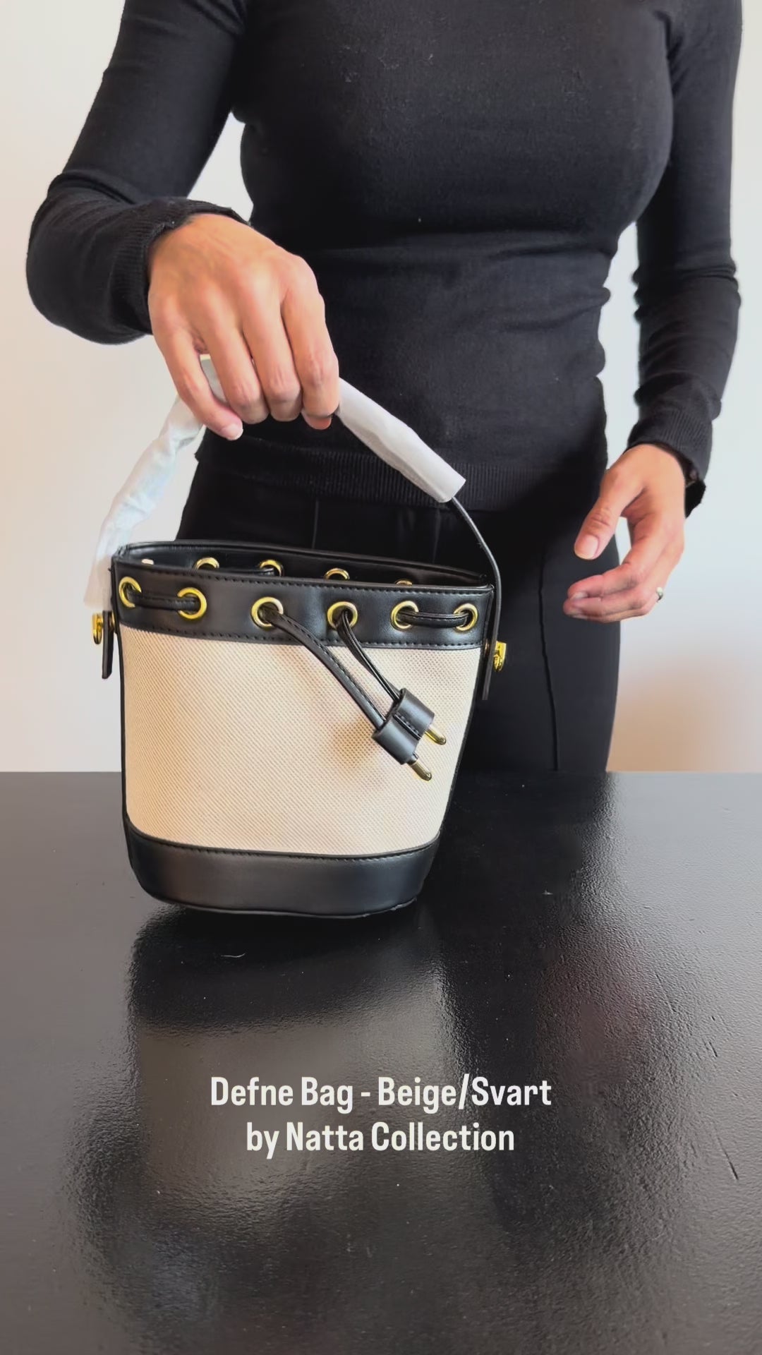 Produktvideo som visar Defne Bag i beige och svart, en bucket bag med handtag, dekorativa öljetter och knytdetaljer, från olika vinklar och i närbild.