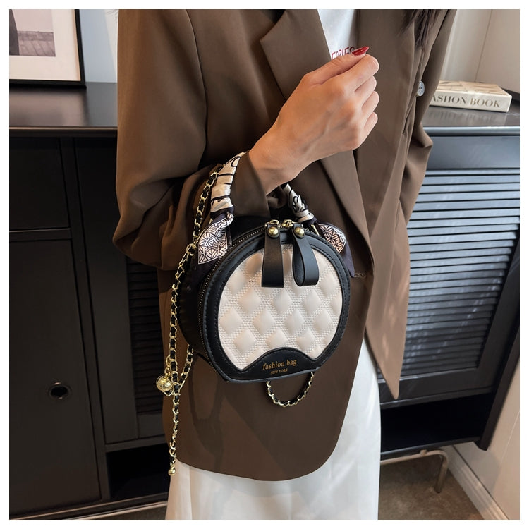 Rund beige och svart crossbodyväska buren över axeln med scarf och guldfärgade detaljer.